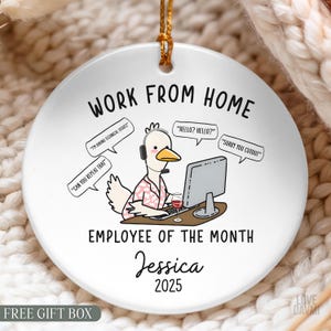 May include: A round white ceramic ornament featuring a cartoon duck wearing a headset and a pink patterned shirt, sitting at a computer with a glass of wine. Text reads: WORK FROM HOME, EMPLOYEE OF THE MONTH, Jessica, 2025, and speech bubbles.