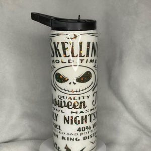 Puede incluir: Botella de agua blanca con tapa negra y boquilla abatible. La botella presenta un dise&ntilde;o de la cara de Jack Skellington y las palabras "Skellin Mold Time" y "Halloween Nights" en letras negras. La botella tiene un acabado brillante.