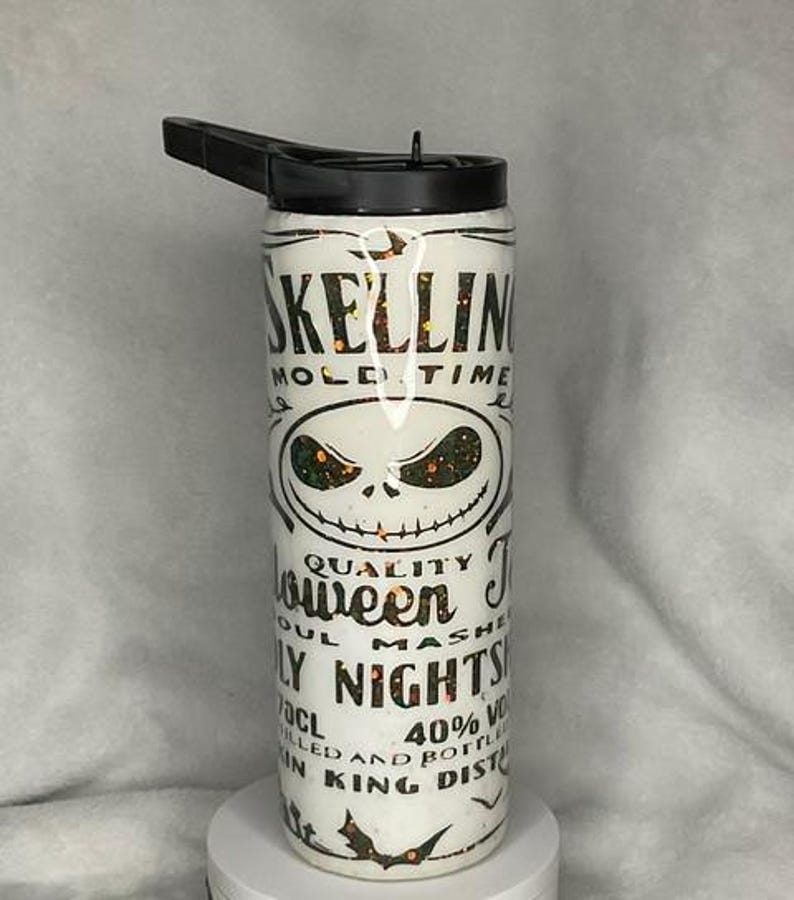 Puede incluir: Botella de agua blanca con tapa negra y boquilla abatible. La botella presenta un dise&ntilde;o de la cara de Jack Skellington y las palabras "Skellin Mold Time" y "Halloween Nights" en letras negras. La botella tiene un acabado brillante.