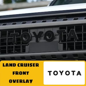 Könnte beinhalten: Schwarzes "TOYOTA" Emblem-Overlay für einen Land Cruiser Frontgrill. Das Bild zeigt die schwarzen Buchstaben des Toyota-Logos auf einem schwarzen Kühlergrill. Die Worte "LAND CRUISER FRONT OVERLAY" stehen in einer gelben Box.