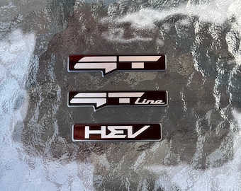GT/GT Line/HEV-emblem med mörkläggningsöverdrag - glansigt svart (för: K5, EV9, EV6, EV5, Sorento, Sportage)