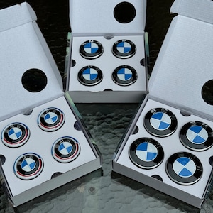 May include: Several sets of BMW wheel center caps, each in a white box. The caps are black with the BMW logo in blue and white. The boxes are open, displaying the caps.