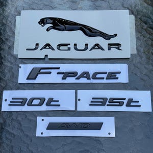 May include: Black Jaguar car emblems and lettering. The image shows a black Jaguar emblem with the word "JAGUAR" below it. Also included are the words "F-PACE", "30t", "35t", and "AWD".