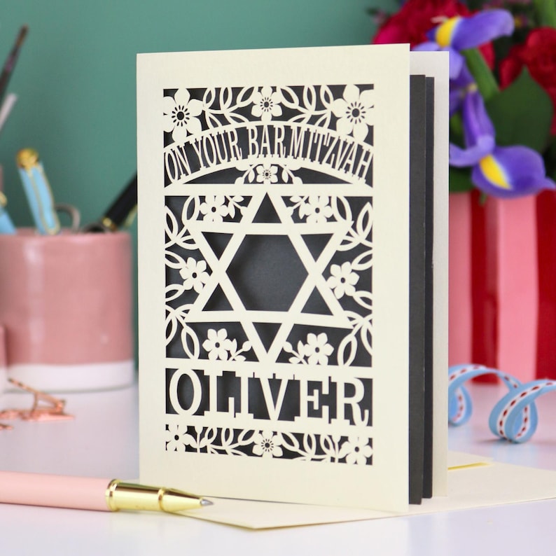 A laser cut Bar Mitzvah card with Star of David design and text "On Your Bar Mitzvah" at the top. The card is personalised with the recipient's name at the bottom and had floral and leaf design elements around the border.