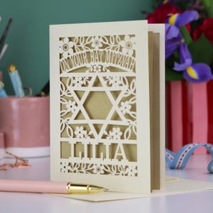 A laser cut Bat Mitzvah card with Star of David design and text "On Your Bat Mitzvah" at the top. The card is personalised with the recipient's name at the bottom and had floral and leaf design elements around the border.