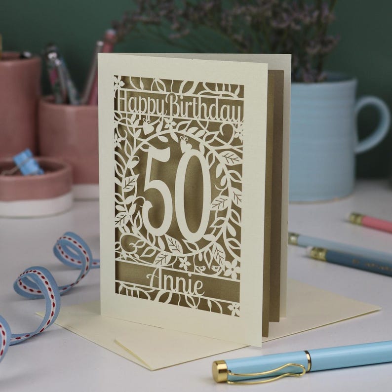 A cut out flower birthday card with cut out floral design and "Happy Birthday" text. The age birthday card is personalised with a cut out name and the age in the centre, surrounded by leaves and flowers