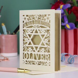 A laser cut Bar Mitzvah card with Star of David design and text "On Your Bar Mitzvah" at the top. The card is personalised with the recipient's name at the bottom and had floral and leaf design elements around the border.