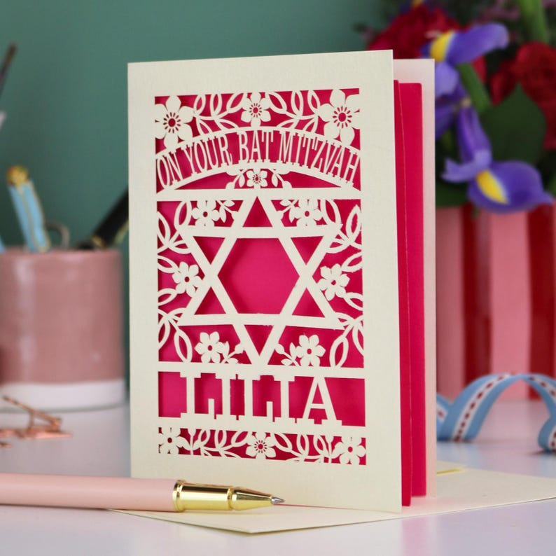 A laser cut Bat Mitzvah card with Star of David design and text "On Your Bat Mitzvah" at the top. The card is personalised with the recipient's name at the bottom and had floral and leaf design elements around the border.