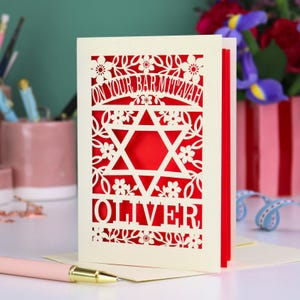 A laser cut Bar Mitzvah card with Star of David design and text "On Your Bar Mitzvah" at the top. The card is personalised with the recipient's name at the bottom and had floral and leaf design elements around the border.