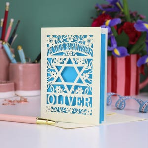 A laser cut Bar Mitzvah card with Star of David design and text "On Your Bar Mitzvah" at the top. The card is personalised with the recipient's name at the bottom and had floral and leaf design elements around the border.