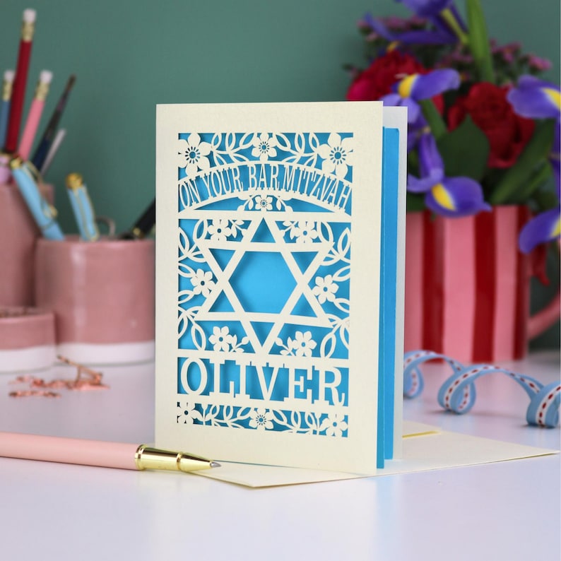 A laser cut Bar Mitzvah card with Star of David design and text "On Your Bar Mitzvah" at the top. The card is personalised with the recipient's name at the bottom and had floral and leaf design elements around the border.