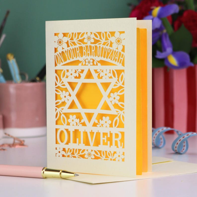 A laser cut Bar Mitzvah card with Star of David design and text "On Your Bar Mitzvah" at the top. The card is personalised with the recipient's name at the bottom and had floral and leaf design elements around the border.