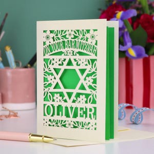 A laser cut Bar Mitzvah card with Star of David design and text "On Your Bar Mitzvah" at the top. The card is personalised with the recipient's name at the bottom and had floral and leaf design elements around the border.