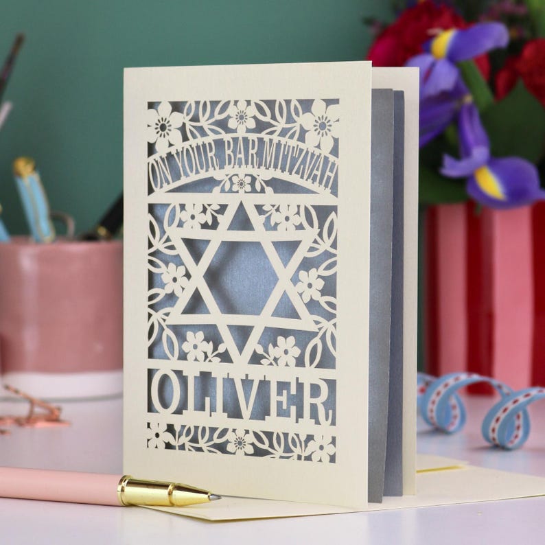A laser cut Bar Mitzvah card with Star of David design and text "On Your Bar Mitzvah" at the top. The card is personalised with the recipient's name at the bottom and had floral and leaf design elements around the border.