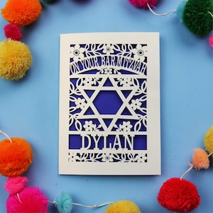 A laser cut Bar Mitzvah card with Star of David design and text "On Your Bar Mitzvah" at the top. The card is personalised with the recipient's name at the bottom and had floral and leaf design elements around the border.