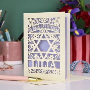 A laser cut Bat Mitzvah card with Star of David design and text "On Your Bat Mitzvah" at the top. The card is personalised with the recipient's name at the bottom and had floral and leaf design elements around the border.