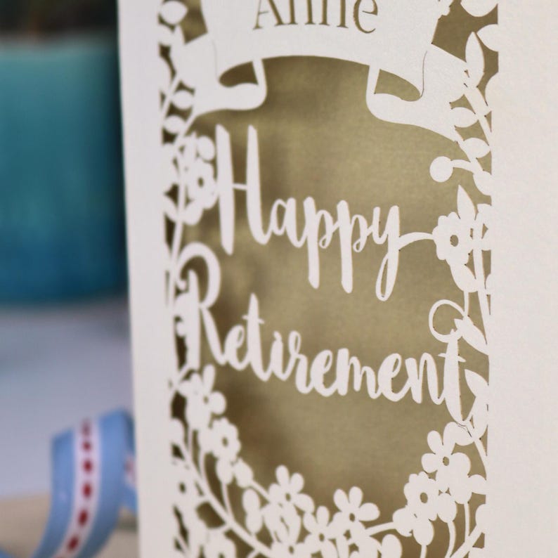 A close up detail of the Happy Retirement font showing the floral border. Shown cut from cream cardstock and gold leaf insert paper