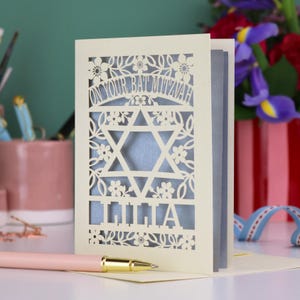 A laser cut Bat Mitzvah card with Star of David design and text "On Your Bat Mitzvah" at the top. The card is personalised with the recipient's name at the bottom and had floral and leaf design elements around the border.