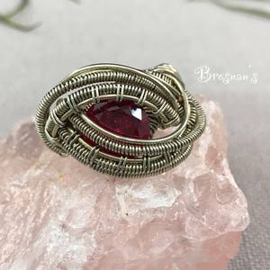 Puede incluir: Un colgante de piedra preciosa roja engastado en alambre de plata. El colgante está hecho de múltiples capas de alambre, creando un diseño de remolino.