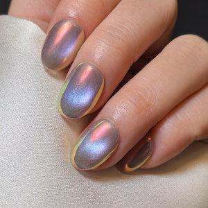 Puede incluir: Primer plano de uñas artificiales iridiscentes de forma ovalada. Las uñas tienen un acabado nacarado multicolor, con tonos de rosa, azul y amarillo. Las uñas son lisas y brillantes, reflejando la luz. Las uñas están en una mano.