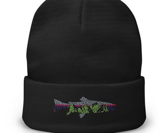 Puede incluir: Gorro negro con un diseño de pez bordado colorido. El pez está detallado con hilo verde, rosa, gris y azul. El gorro es de estilo clásico, con vuelta, adecuado para el frío.