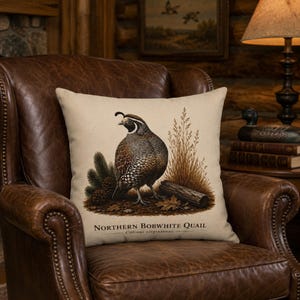 May include: A square throw pillow with a beige fabric cover featuring a detailed illustration of a Northern Bobwhite Quail standing near a log, pine cones, and tall grass. The text Northern Bobwhite Quail Colinus virginianus is printed below.
