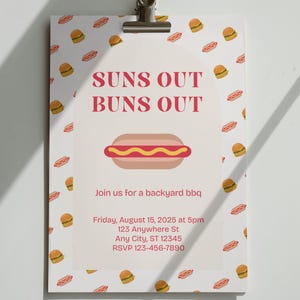 May include: A white invitation card with the text "SUNS OUT BUNS OUT" and a hot dog illustration. The card is decorated with small burger and hot dog graphics. It is clipped to a white surface.