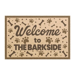 May include: A rectangular doormat with a tan background and a brown border. The mat features paw prints and bone shapes scattered across the surface. The words "Welcome to THE BARKSIDE" are printed in brown.