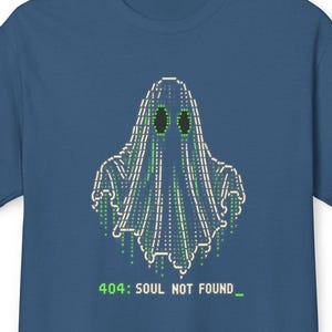 May include: A blue short-sleeved t-shirt featuring a graphic of a ghost composed of white and green digital code characters. Below the ghost, the text reads 404: SOUL NOT FOUND with a green underscore cursor, mimicking a computer terminal interface.