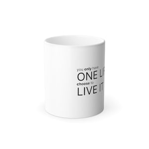 以下が含まれることがあります： 「you only have ONE LIFE choose to LIVE IT」という黒い文字がプリントされた白いセラミック製のマグカップ。マグカップは滑らかな質感の円筒形で、持ち手のないシンプルなデザインとなっており、引用文がはっきりと表示されています。