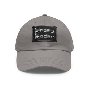 Könnte beinhalten: Graue Baseballkappe mit gebogenem Schirm. Die Kappe hat einen schwarzen rechteckigen Aufnäher mit dem weißen Text "Dress Coder". Der Hut ist aus einem weichen Material gefertigt und hat einen klassischen, lässigen Stil.