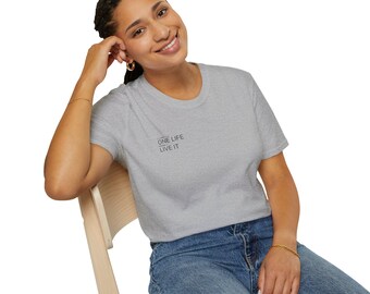May include: A light gray t-shirt with the text "ONE LIFE LIVE IT" printed in black. The shirt is worn with blue jeans. The person is sitting on a wooden chair.