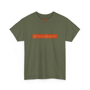 Peut inclure: T-shirt vert olive avec le texte "DressCoder" en lettres orange. Le t-shirt à manches courtes est fait d'une matière douce et convient aux tenues décontractées. Le t-shirt est présenté sur fond blanc.