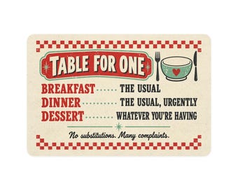 Può includere: Un cartello rettangolare con bordo a scacchi rossi e bianchi che presenta il testo TABLE FOR ONE, una ciotola con un cuore, una forchetta e un coltello. Elenca BREAKFAST, DINNER e DESSERT con testo umoristico, terminando con No substitutions. Many complaints.