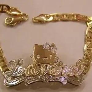 May include: A gold-toned bracelet with a chain link design. The bracelet features a charm of Hello Kitty and the name "Laura" in a cursive font. The charm and name are in a silver color.