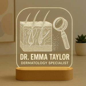 May include: A clear acrylic desk lamp with a wooden base. The lamp features an etched design of a skin cross-section, hair follicles, and a magnifying glass. The text reads "DR. EMMA TAYLOR DERMATOLOGY SPECIALIST".