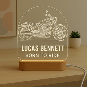 May include: A motorcycle-themed night light with a wooden base. The clear acrylic panel features a detailed line drawing of a motorcycle and the text "LUCAS BENNETT BORN TO RIDE" in white. The light emits a warm glow.