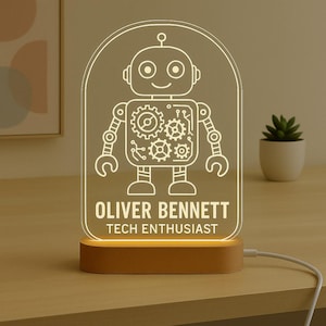 May include: A personalized LED night light featuring a robot design with gears and circuits. The light is engraved with the name "OLIVER BENNETT" and the text "TECH ENTHUSIAST". The light sits on a wooden base.