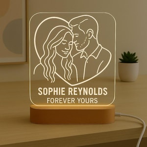 May include: A personalized LED night light featuring a couple's portrait within a heart shape. The names "SOPHIE REYNOLDS" and the phrase "FOREVER YOURS" are displayed below the image. The light sits on a wooden base.