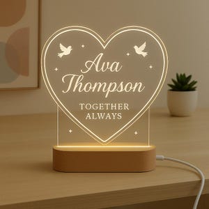 May include: A heart-shaped LED night light with the name "Ava Thompson" and the words "Together Always" engraved on it. The light has a wooden base and features two bird silhouettes and star accents.