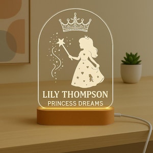 May include: A personalised princess night light with a wooden base. The clear acrylic panel features a princess silhouette, crown, and star wand design. The text reads "LILY THOMPSON PRINCESS DREAMS".