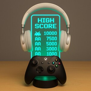 May include: A gaming-themed night light with a glowing green display showing "HIGH SCORE" and points. A black game controller is positioned below the display, and white headphones are placed above. The design is reminiscent of a retro arcade game.
