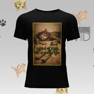 Puede incluir: Camiseta negra con un diseño gráfico humorístico que representa un gato y un extraterrestre, con el texto "I need a nap... or a new life." Ilustraciones de gatos y huellas de patas en el fondo.