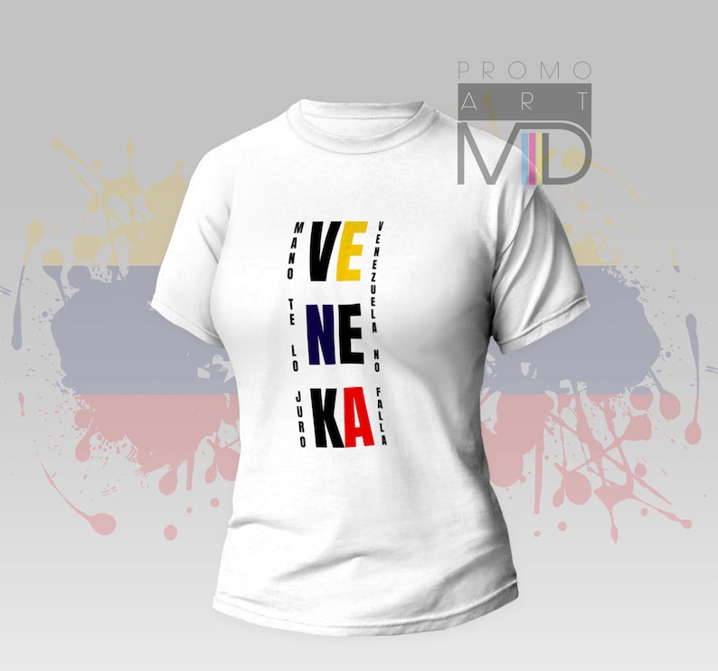 May include: White t-shirt with the word "VENEZUELA" vertically aligned in black, yellow, blue, and red. The shirt has a crew neck and short sleeves. The design includes additional text on the left and right sides of the main text.