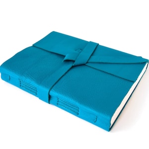 May include: A teal leather-bound journal with a leather strap closure. The journal is closed and lying flat on a white surface.