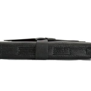 May include: A black leather journal with a strap closure. The journal has a textured surface and is closed.