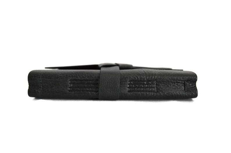 May include: A black leather journal with a strap closure. The journal has a textured surface and is closed.