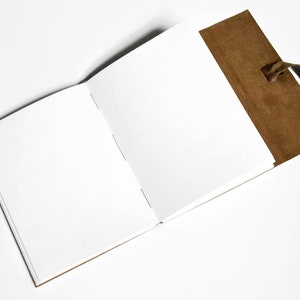 K&ouml;nnte beinhalten: Ein braunes ledergebundenes Tagebuch mit einer leeren wei&szlig;en Seite, die aufgeschlagen ist. Das Tagebuch hat einen braunen Lederriemen mit einem Quasten.