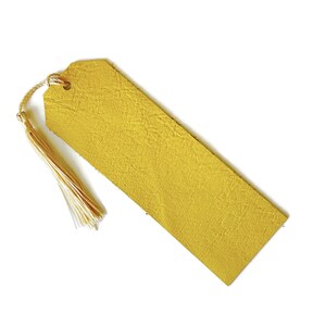 May include: A yellow leather bookmark with a tassel. The bookmark is made of a textured leather and has a hole at the top for a ribbon or string.