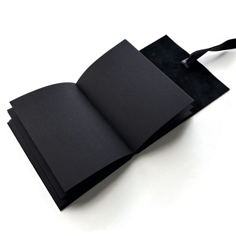 May include: A black leather-bound journal with a black ribbon closure. The journal is open to reveal blank pages.